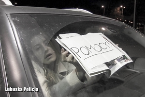 kobieta trzyma przy szybie samochodu kartkę z napisem pomocy